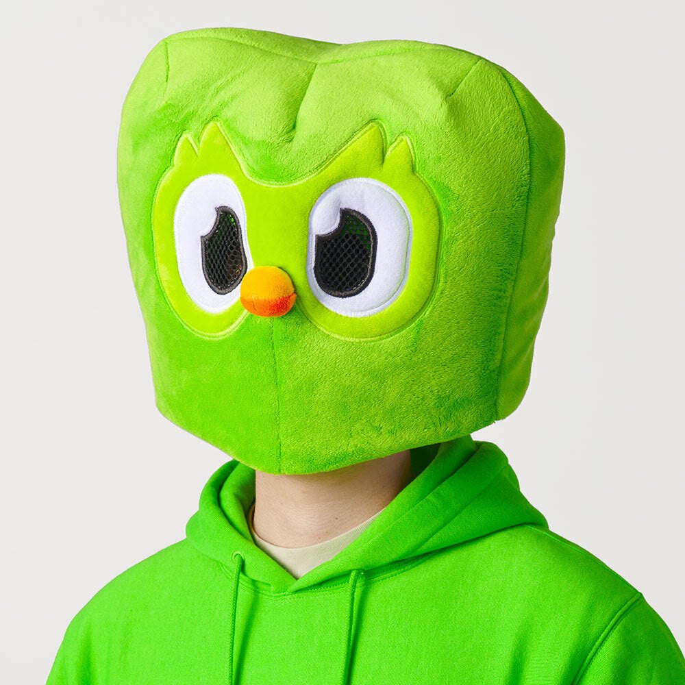 A person in a green hoodie wearing a plush Duo the owl mask